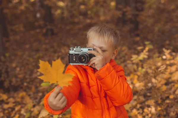 Pojke med retrokamera som fotograferar utomhus i höstnaturen. Fritid och fotografer koncept — Stockfoto