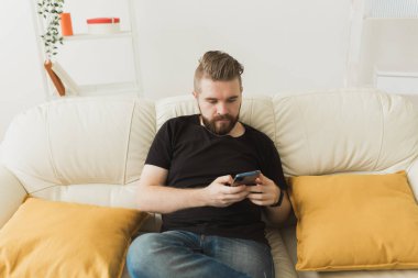 Evde cep telefonu kullanan yakışıklı bir hippi. İletişim eğlence ve teknoloji kavramı