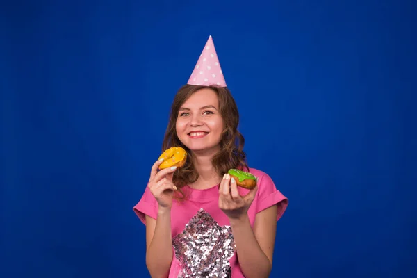 파란 배경에 도넛을 달고 다니는 예쁘고 재미있는 소녀. 건강에 좋지 않은 식사, 정크푸드, 파티 및 축하의 개념 — 스톡 사진