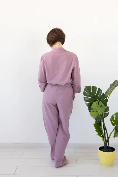 Zadní pohled na ženu oblečenou v krásném barevném pyžamu, vydávající se za modelku ve svém obýváku. Pohodlné spací oděvy, domácí relaxace a ženský módní koncept. — Stock fotografie
