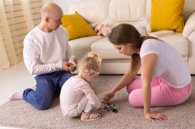 Koklear implantı olan çocuk evde anne ve babasıyla eğleniyor. Sağırlık ve tıbbi teknoloji kavramı.