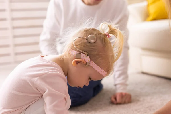 A gyerek cochleáris implantátumokkal otthon játékokkal játszik. Süketség és orvostechnikai koncepció. — Stock Fotó
