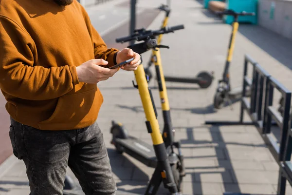 Zbliżenie samca za pomocą smartfona po jeździe skuterem elektrycznym w mieście. Innowacyjny transport — Zdjęcie stockowe