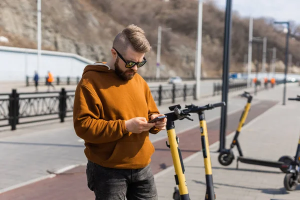 Man met behulp van smartphone na het rijden met elektrische scooter in de stad. Innovatief vervoer — Stockfoto