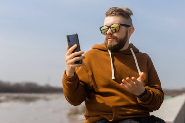 Milenyum sakallı adam şehrin dışındaki cep telefonundan video görüşmesi yapıyor. Video çağrısı akıllı telefon ve teknoloji kavramı