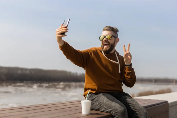 Sakallı adam baharın tadını çıkarıyor ve akıllı telefon kullanarak gezinti alanında selfie çekiyor. Teknoloji boş zaman ve gen z konsepti — Stok fotoğraf