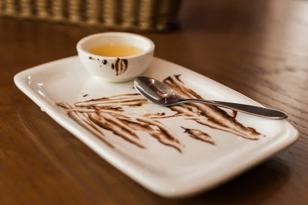 Töm skålen efter tårta med sås och sked. Stökig tallrik på ett bord i caféet — Stockfoto