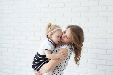 Anne bebeğini işitme cihazıyla ve koklear implantlarla beyaz tuğla duvarda tutuyor. Reklam için yeri ve yeri var. Sağır ve sağlık kavramı