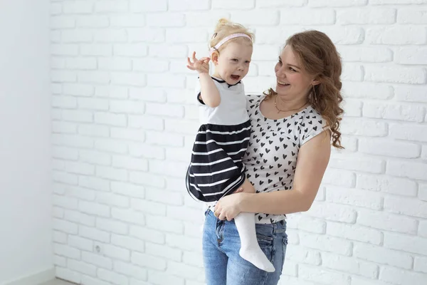 Anne bebeğini işitme cihazıyla ve koklear implantlarla beyaz tuğla duvarda tutuyor. Reklam için yeri ve yeri var. Sağır ve sağlık kavramı — Stok fotoğraf
