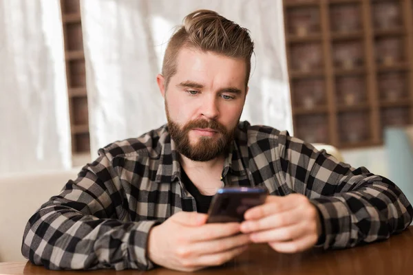 Hombre sosteniendo dispositivo de teléfono inteligente digital moderno y charlando en las redes sociales. Chico enviando un mensaje en celular mientras está sentado en la mesa en la cafetería — Foto de Stock