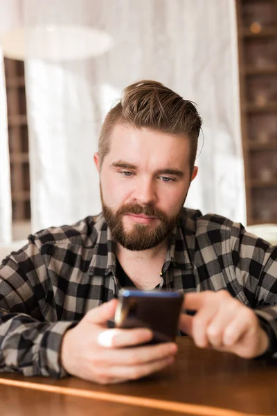 Joven chico hipster buscando noticias de las redes sociales leer a través de teléfono inteligente en tiempo libre en la cafetería — Foto de Stock