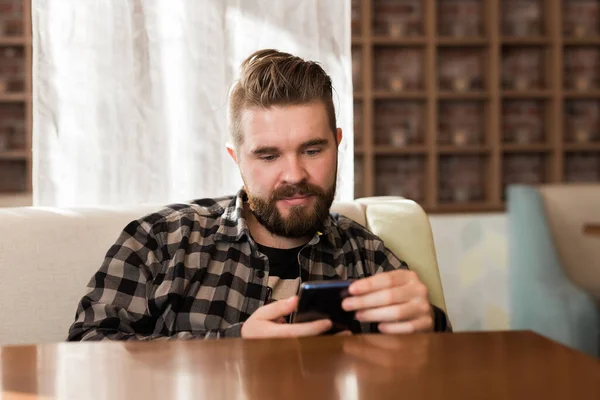 Joven chico hipster buscando noticias de las redes sociales leer a través de teléfono inteligente en tiempo libre en la cafetería — Foto de Stock