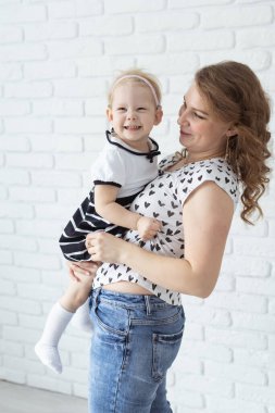 Anne, çocuğunu işitme cihazı ve koklear implantlarla beyaz tuğla duvarda tutuyor. Sağır ve sağlık kavramı