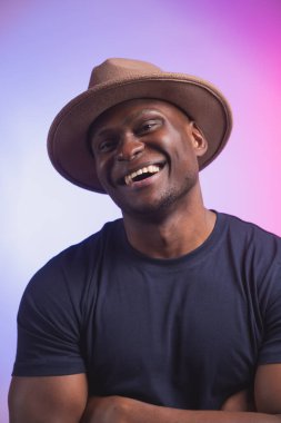 Gülümseyen mutlu Amerikalı Afrikalı adam pembe ve mor arka planda şık bir şapka giyiyor. Şenlikli ve parti konsepti