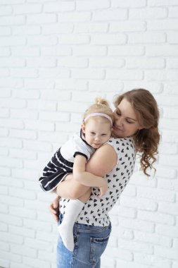 Anne, çocuğunu işitme cihazı ve koklear implantlarla beyaz tuğla duvarda tutuyor. Sağır ve sağlık kavramı