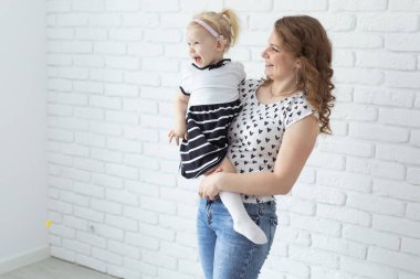 Anne bebeğini işitme cihazıyla ve koklear implantlarla beyaz tuğla duvarda tutuyor. Reklam için yeri ve yeri var. Sağır ve sağlık kavramı