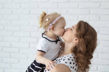 Anne, çocuğunu işitme cihazı ve koklear implantlarla beyaz tuğla duvarda tutuyor. Sağır ve sağlık kavramı