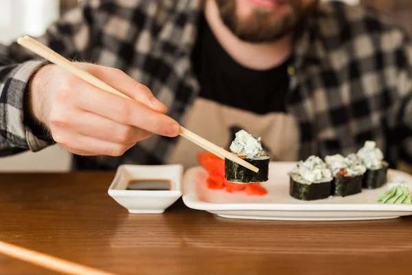 Zamykanie bułek sushi na stole w restauracji. Człowiek jedzący sushi używając bambusowych pałeczek. Kuchnia japońska — Zdjęcie stockowe