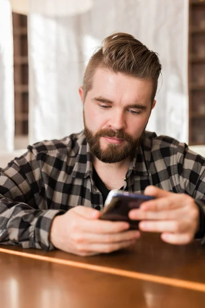 Hombre sonriente usando teléfono inteligente en la cafetería moderna, que chatear Mensajería en línea en el móvil. Concepto de redes sociales y millennials — Foto de Stock