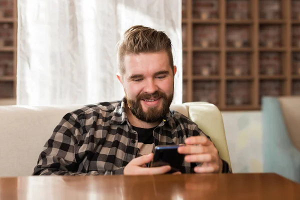 Hombre sosteniendo dispositivo de teléfono inteligente digital moderno y charlando en las redes sociales. Chico enviando un mensaje en celular mientras está sentado en la mesa en la cafetería — Foto de Stock