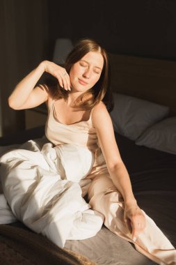 Kız sabah uyanıyor yatakta esneme hareketleri yapıyor ve pencereden güneş parlıyor. Mutlu genç kadın yeni güneşli günü selamlıyor