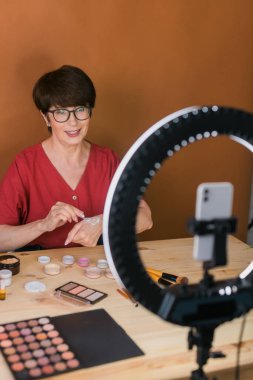 Beauty and cosmetics e-commerce and blogging concept - professional mature female make up artist testing new cosmetics recording video review on cosmetic products at home