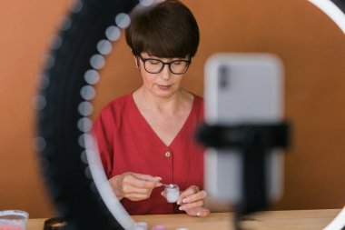 Beauty and cosmetics e-commerce and blogging concept - professional mature female make up artist testing new cosmetics recording video review on cosmetic products at home