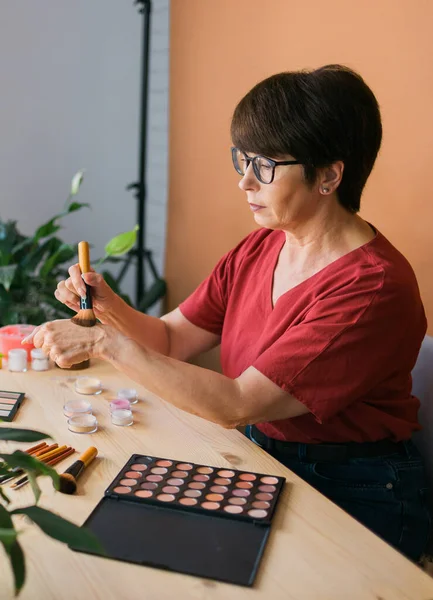 Beauty and cosmetics e-commerce and blogging concept - professional mature female make up artist testing new cosmetics recording video review on cosmetic products at home