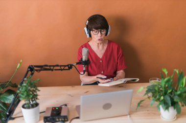 Middle-aged female radio presenter talking into the microphone and reading news - radio broadcast online concept
