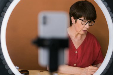 Beauty and cosmetics e-commerce and blogging concept - professional mature female make up artist testing new cosmetics recording video review on cosmetic products at home