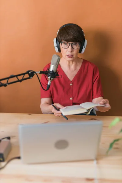 Portrait of mature woman wearing headphones and talking at online radio station - podcast and broadcast concept — Stock fotografie