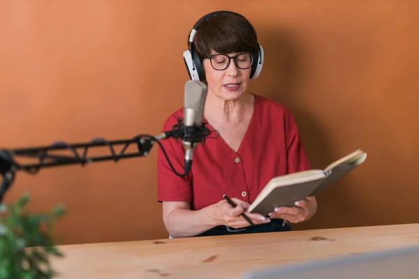 Middle-aged female radio presenter talking into the microphone and reading news - radio broadcast online concept — Stockfoto