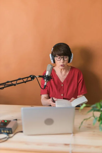 Middle-aged female radio presenter talking into the microphone and reading news - radio broadcast online concept — Stock fotografie
