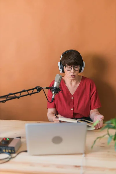 Portrait of mature woman wearing headphones and talking at online radio station - podcast and broadcast concept — Stock fotografie