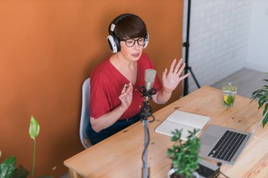 Middle-aged female radio presenter talking into the microphone and reading news - radio broadcast online concept