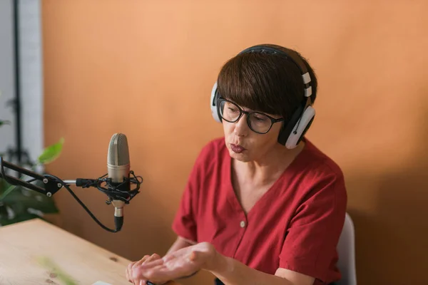 Portrait of mature woman wearing headphones and talking at online radio station - podcast and broadcast concept — Stock fotografie