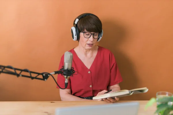 Mature woman making podcast recording for her online show. Attractive business woman using headphones front of microphone for a radio broadcast — Stockfoto