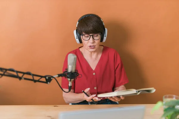 Portrait of mature woman wearing headphones and talking at online radio station - podcast and broadcast concept — Stock fotografie