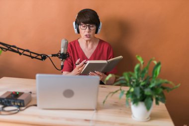 Portrait of mature woman wearing headphones and talking at online radio station - podcast and broadcast concept