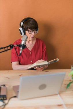 Mature woman making podcast recording for her online show. Attractive business woman using headphones front of microphone for a radio broadcast