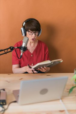 Portrait of mature woman wearing headphones and talking at online radio station - podcast and broadcast concept
