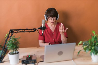 Middle-aged female radio presenter talking into the microphone and reading news - radio broadcast online concept