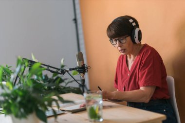 Mature woman making podcast recording for her online show. Attractive business woman using headphones front of microphone for a radio broadcast
