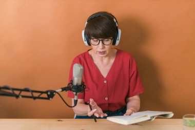 Middle-aged female radio presenter talking into the microphone and reading news - radio broadcast online concept