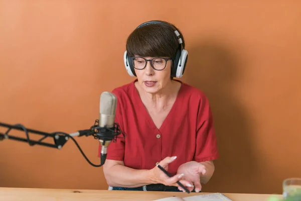 Middle-aged female radio presenter talking into the microphone and reading news - radio broadcast online concept — Stockfoto