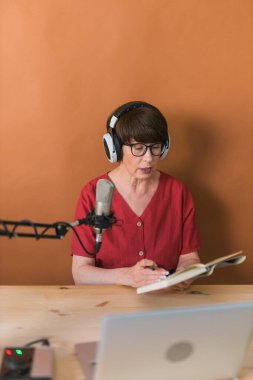 Middle-aged female radio presenter talking into the microphone and reading news - radio broadcast online concept