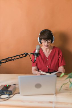 Middle-aged female radio presenter talking into the microphone and reading news - radio broadcast online concept
