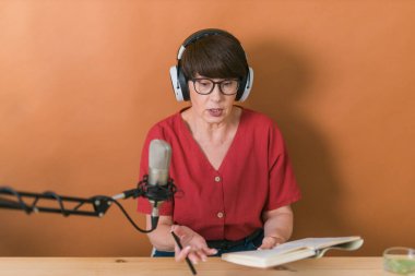 Mature woman making podcast recording for her online show. Attractive business woman using headphones front of microphone for a radio broadcast
