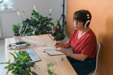 Middle-aged female radio presenter talking into the microphone and reading news - radio broadcast online concept