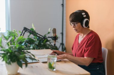 Middle-aged female radio presenter talking into the microphone and reading news - radio broadcast online concept